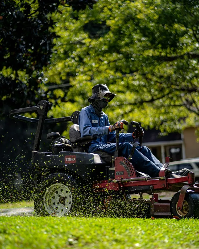 A zero-turn mower cutting a wide green residential lawn